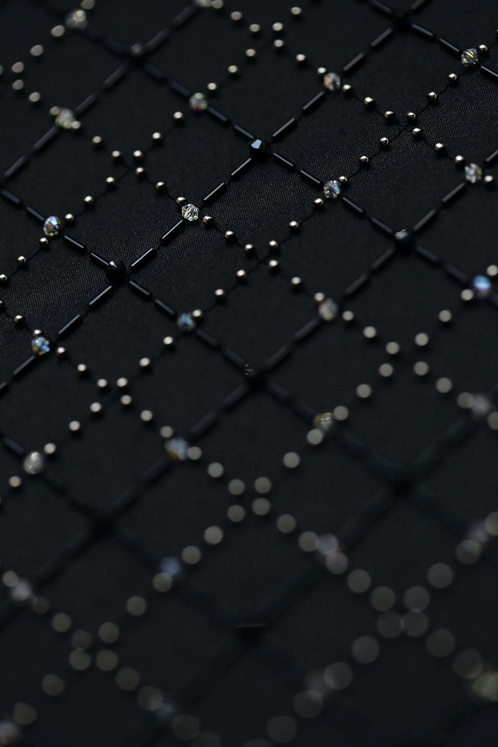 Primer plano de la cuadrícula negra bordada a mano con cristales de Celaeno, estrella de las Pléyades.