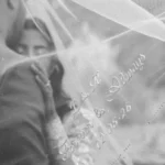 Fotografía en blanco y negro de los recién casados tras un velo de novia bordado de forma personalizada.
