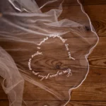 Voile de mariée personnalisé Celestia déployé sur un parquet, mettant en valeur sa délicate broderie en forme de cœur.