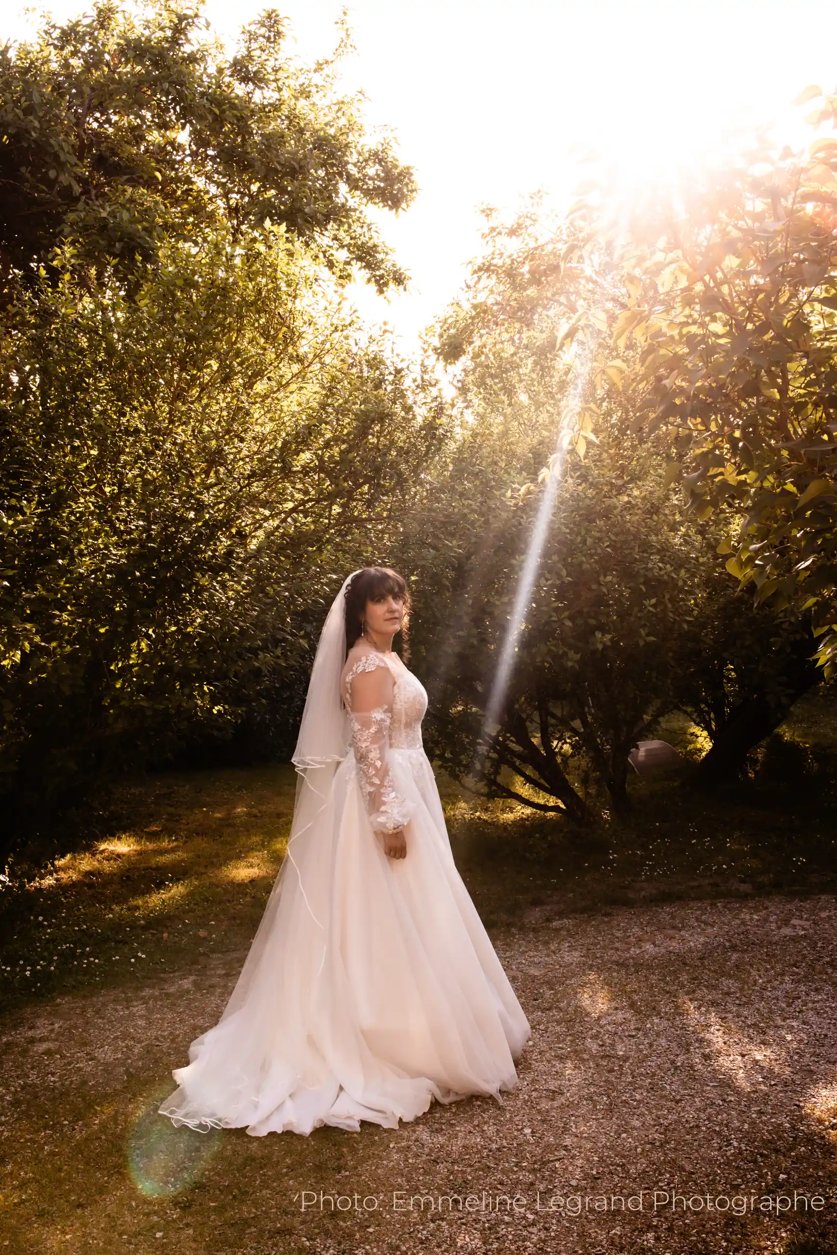 Novia con el velo personalizado Celestia bordado a mano al atardecer, en un paisaje de bosque suavemente iluminado.