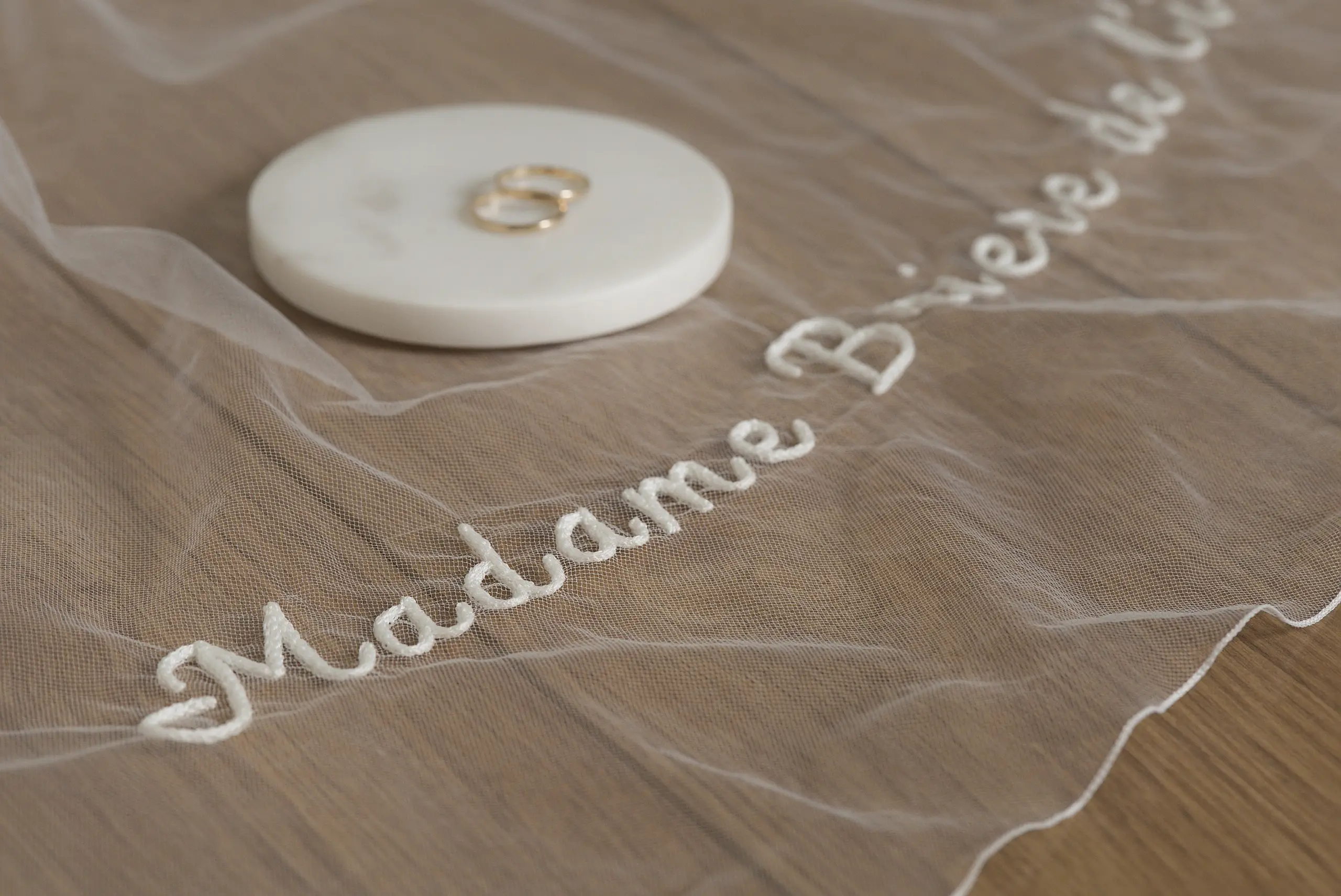 Voile de mariée brodé et minimaliste avec un prénom personnalisé, présenté avec deux alliances sur un disque en marbre.