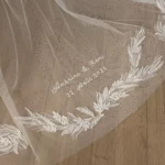 Voile de mariée de luxe Elara avec les noms des mariés et leur date de mariage brodés à la main sur un parquet.
