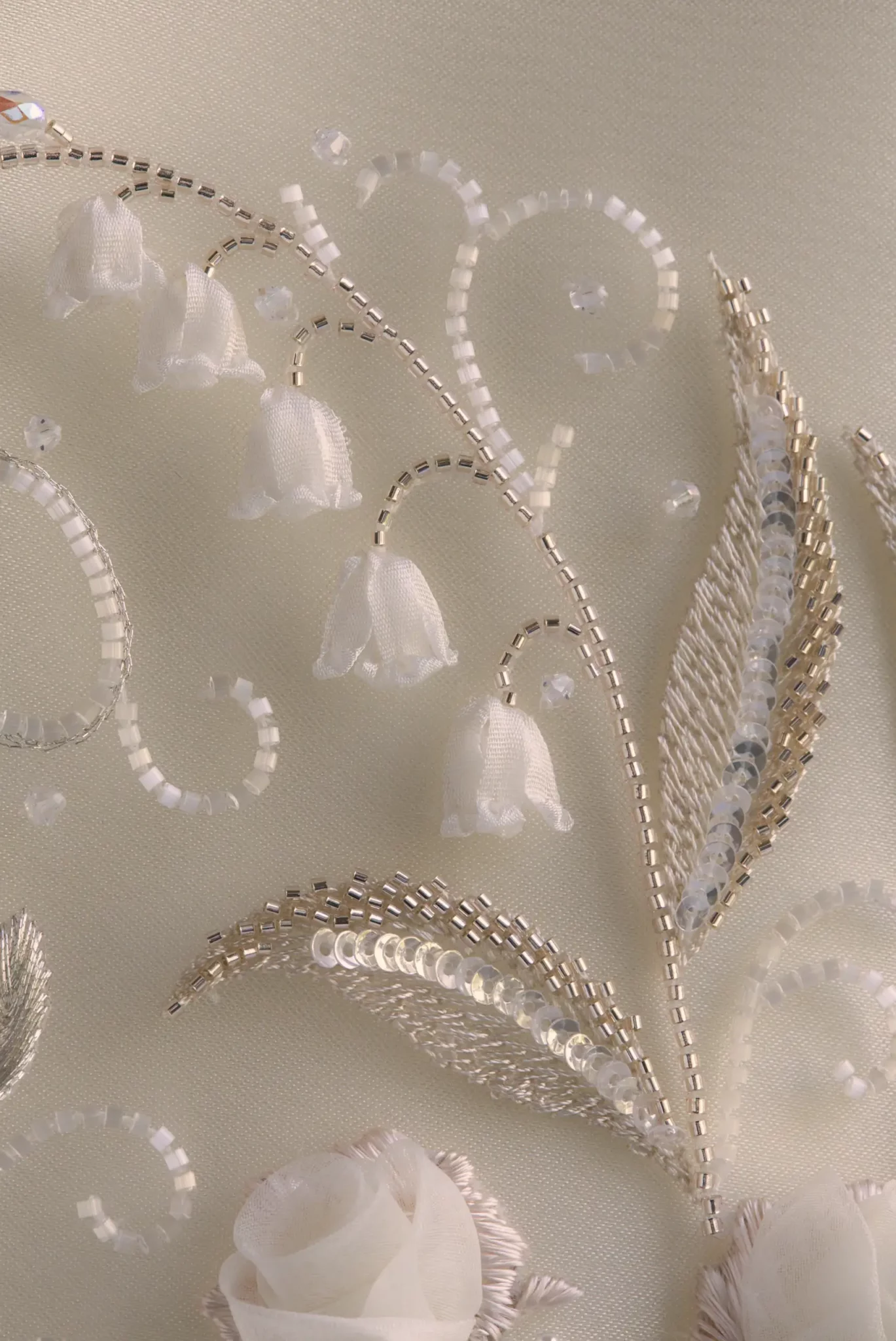 Détail en macro d’une broderie de mariée sur mesure sur tulle, mettant en valeur le délicat muguet et ses feuilles.