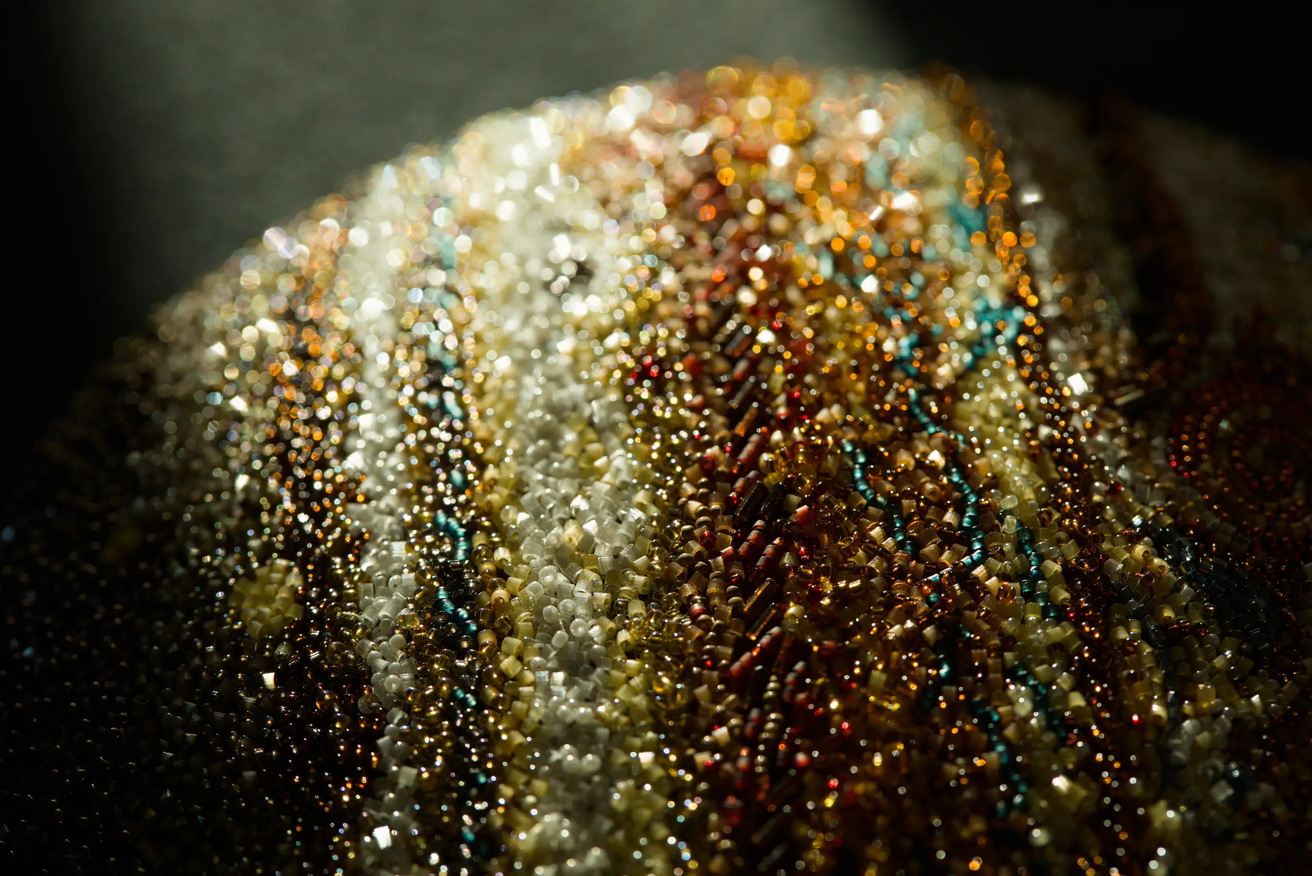 Detalle macro de una obra original de Júpiter bordado, destacando sus cuentas, texturas y detalles llenos de luz.