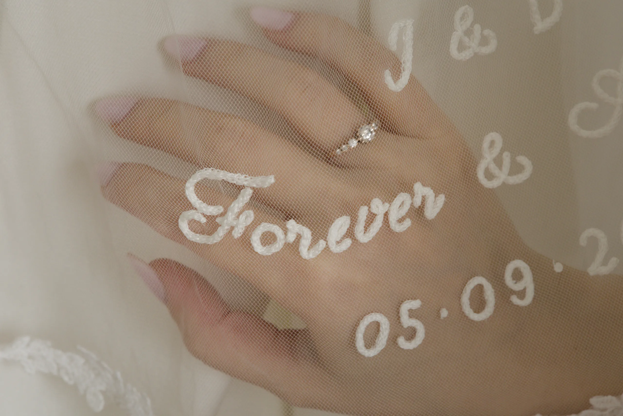 Macro view of a short embroidered bridal veil with a wedding ring visible through the sheer tulle.