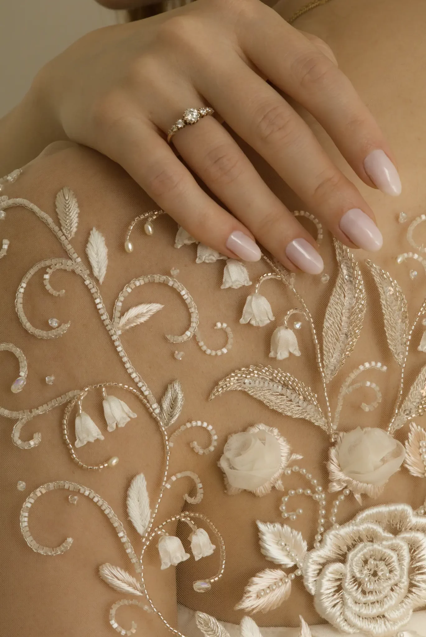A hand with a wedding ring touches a bespoke bridal embroidery on sheer tulle creating a delicate tattoo effect on the skin