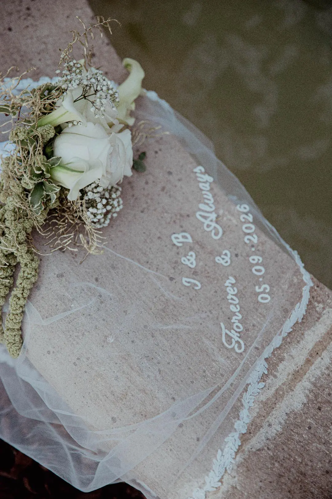 Voile de mariée brodé court posé sur un tronc, avec le bouquet de la mariée sur le tulle délicatement brodé.