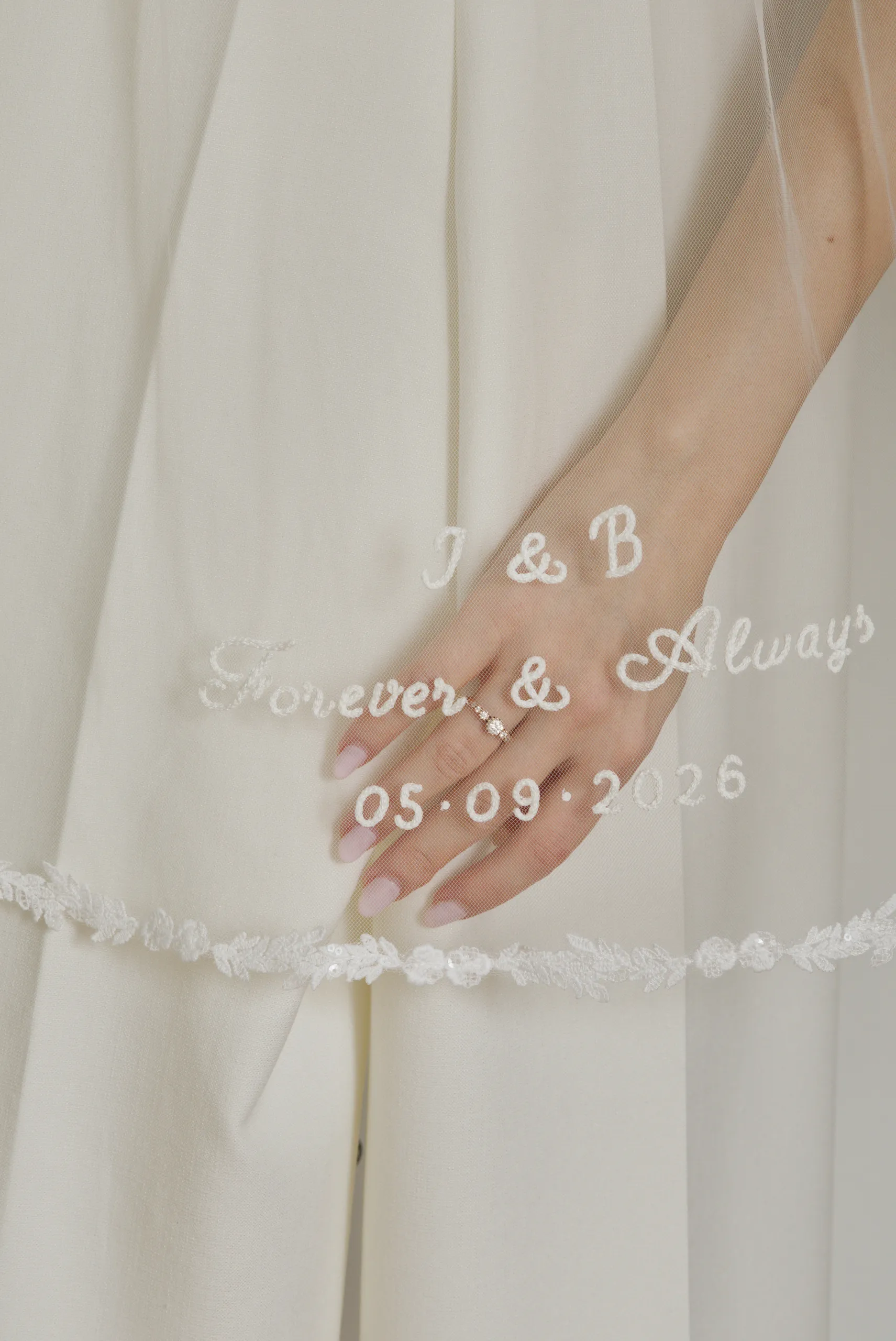 Gros plan de la broderie du voile Halo sur tulle transparent, avec une alliance visible à travers le voile.